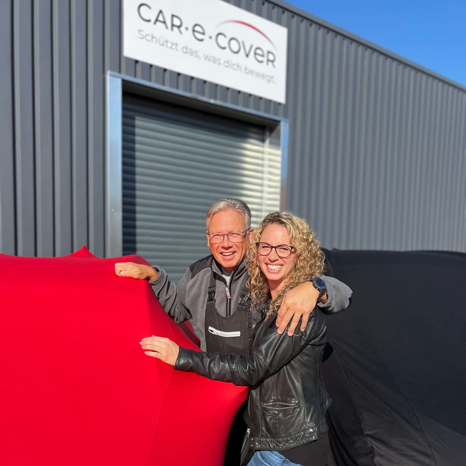 Das Team von Car-e-Cover vor dem Firmengebäude mit roter und schwarzer Auto-Abdeckung – deutscher Hersteller mit über 20 Jahren Erfahrung
